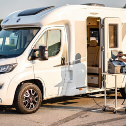 Camping-car moderne stationné sur une aire ensoleillée, avec un technicien contrôlant la climatisation de la cabine à l’aide d’une station de diagnostic.